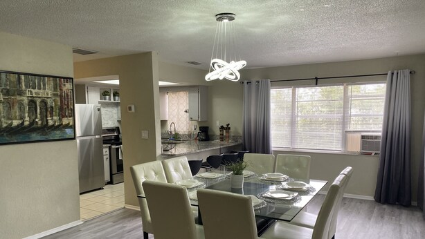 A dining area with a glass table, white chairs, and a modern chandelier. - Orlando Spacious Home Near Universal (Orlando)