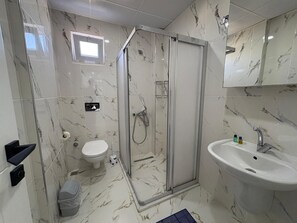 Un baño con ducha envuelta en vidrio, inodoro, lavabo y espejo.