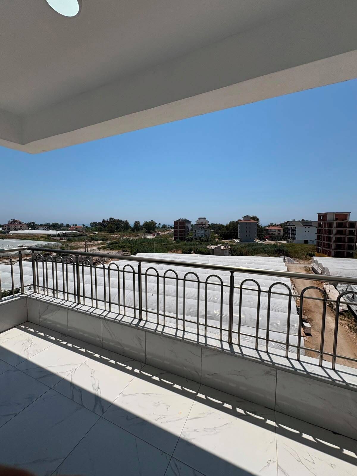 A balcony with a metal railing, a tiled floor, and a clear view of the surrounding buildings and landscape.