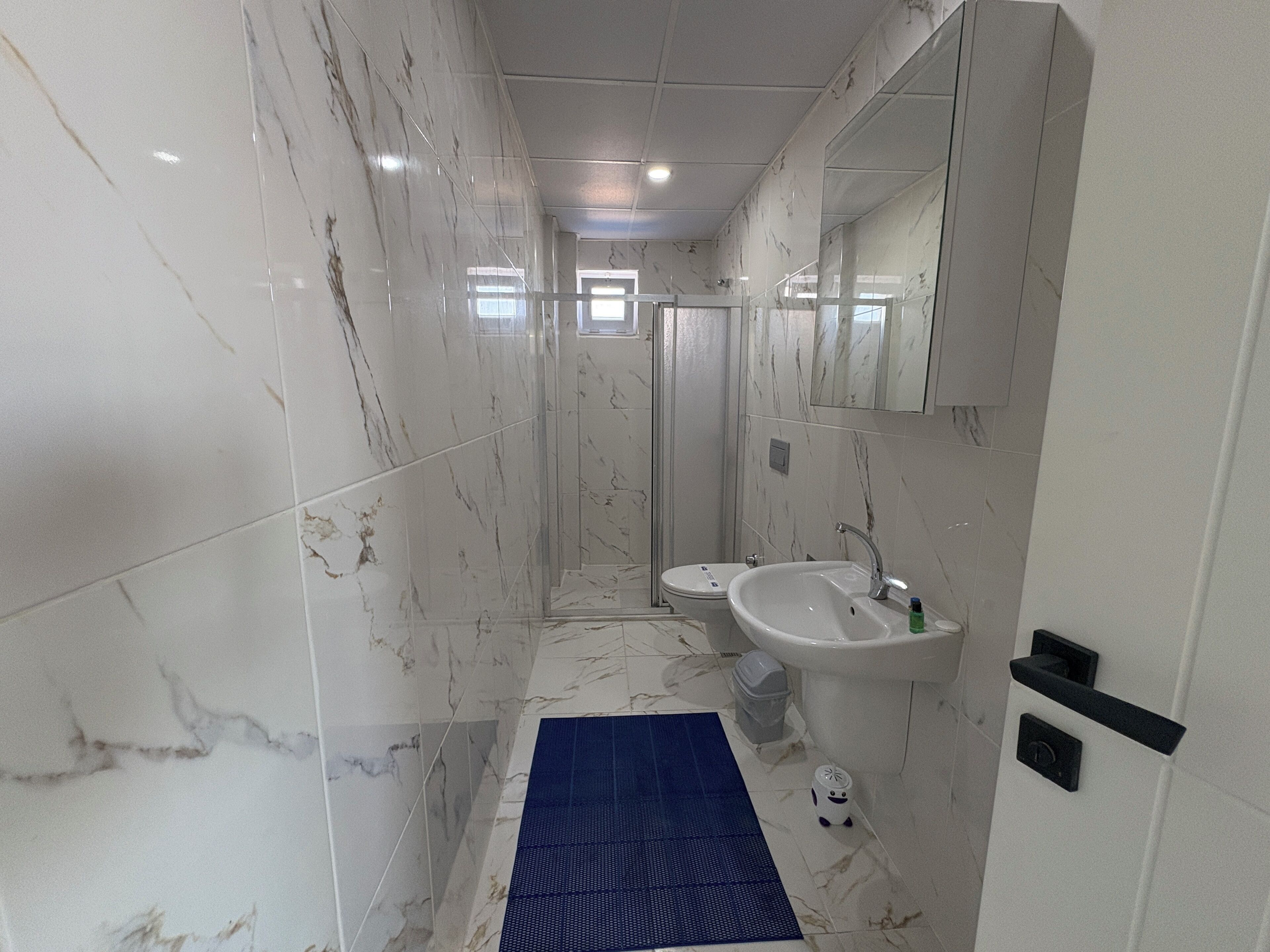 A modern bathroom with white marble tiles, a white sink, and a blue mat on the floor.