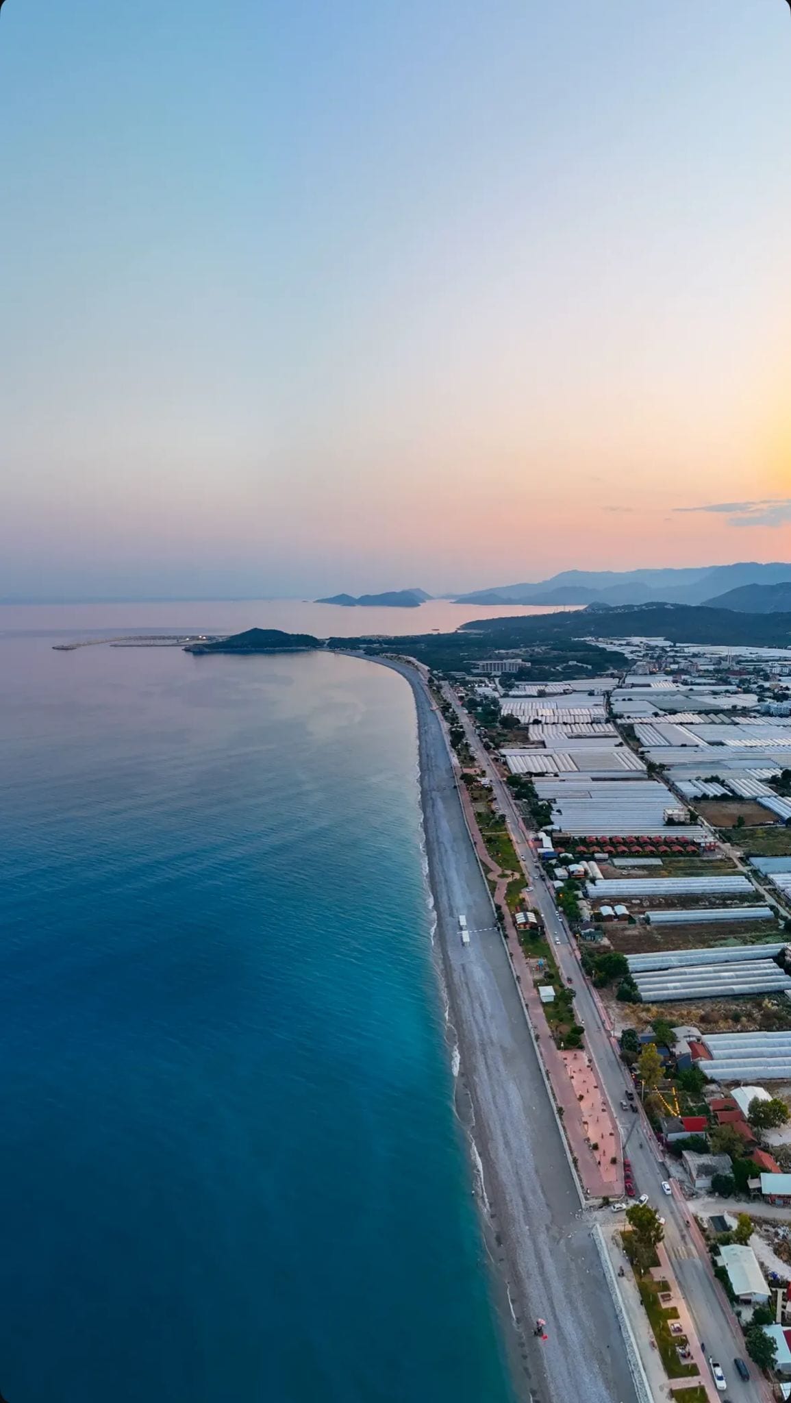 An aerial view of a coastal area with a long stretch of beach and adjacent industrial buildings.