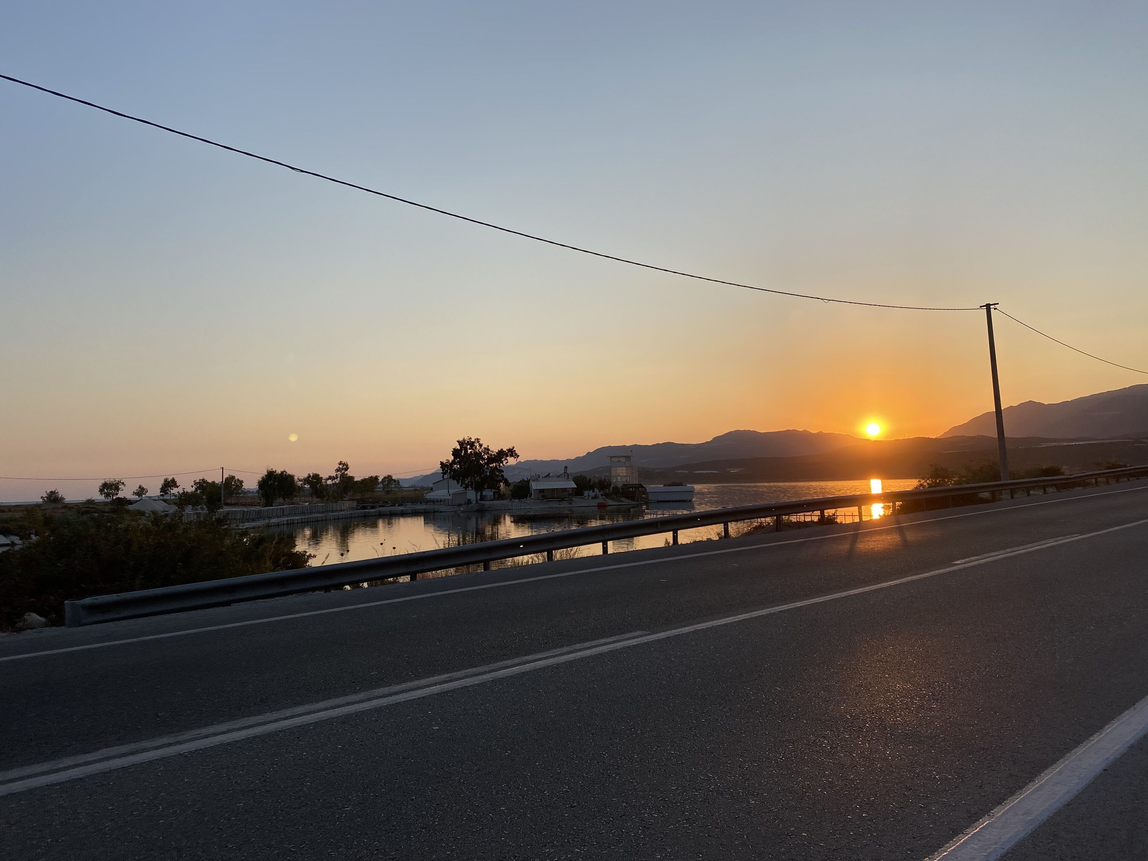 A highway with a sunset in the background, a bridge, and a body of water.