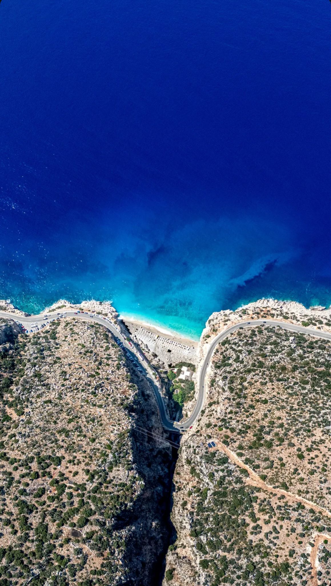 Luchtbeeld van een kustweg met een strand en rotsachtig terrein.