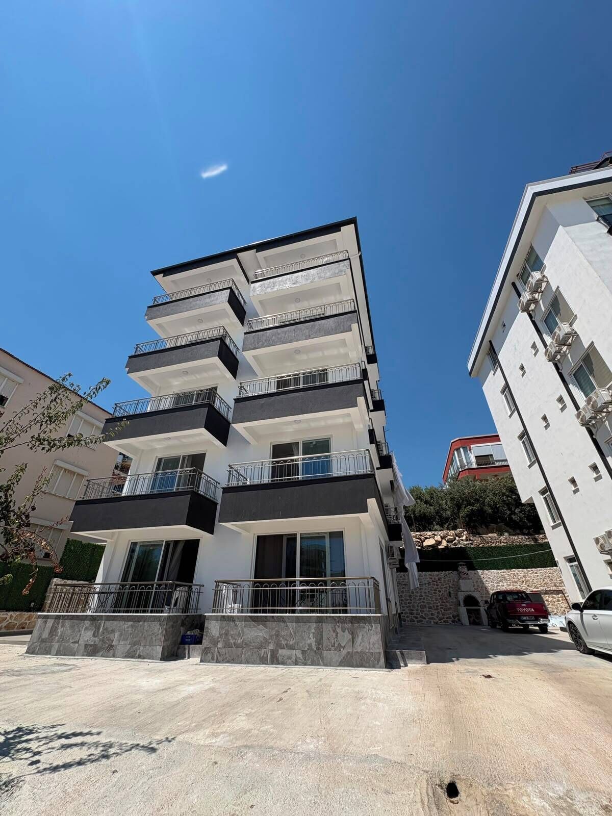 Un edifici residencial de diversos pisos amb balcons, una base de pedra i un cel clar.