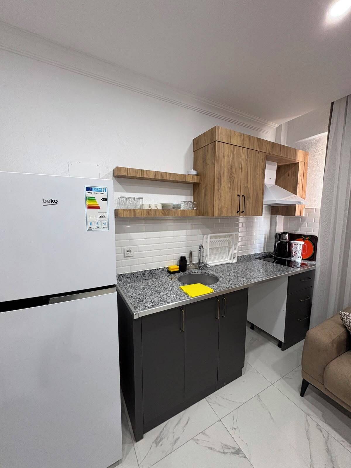 A compact kitchen with a refrigerator, a sink, and wooden cabinets.