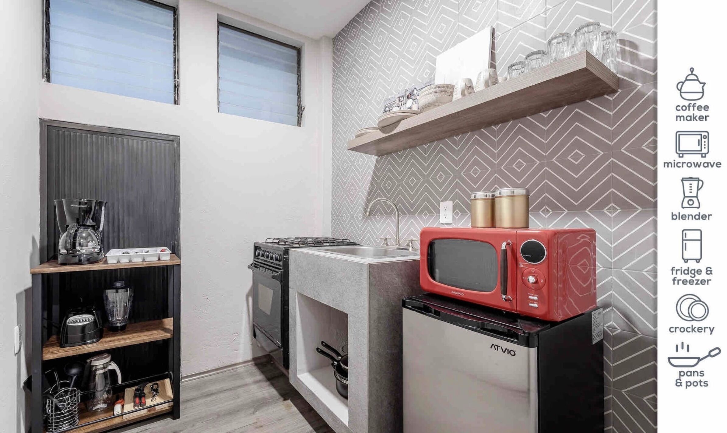 Cocina compacta con estufa a gas, microondas rojo y refrigerador. Se observan repisas con utensilios de cocina y una cafetera.