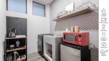 Cocina compacta con estufa a gas, microondas rojo y refrigerador. Se observan repisas con utensilios de cocina y una cafetera.
