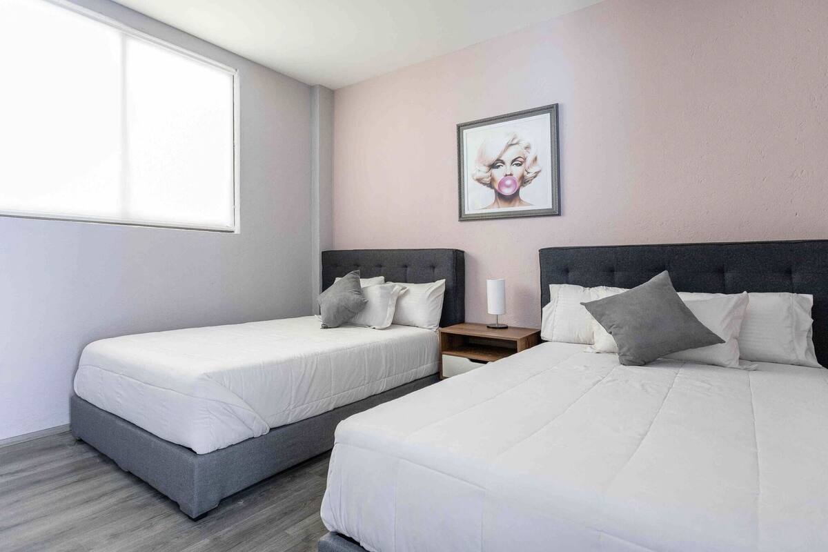 A hotel room with two beds, a window, and a framed picture on the wall.