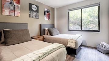 A bedroom with two beds, a nightstand, a window with a view of trees, and wall art including a clock and a 'create' sign.