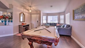 Une table de billard dans un salon, avec un canapé et un tableau accroché au mur.