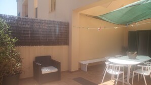 Un patio con una mesa y sillas blancas, un sofá negro, una planta en maceta y un tendedero.