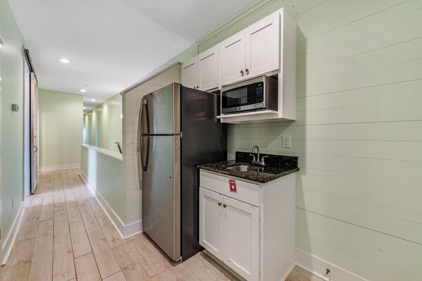 A kitchen with white cabinets, a stainless steel refrigerator, a microwave, and a granite countertop.