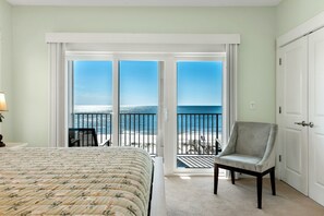 A hotel room with a bed, a chair, and a view of the beach through a sliding door.