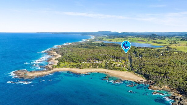 Vista aérea de una zona costera con playa, colinas boscosas y una masa de agua.