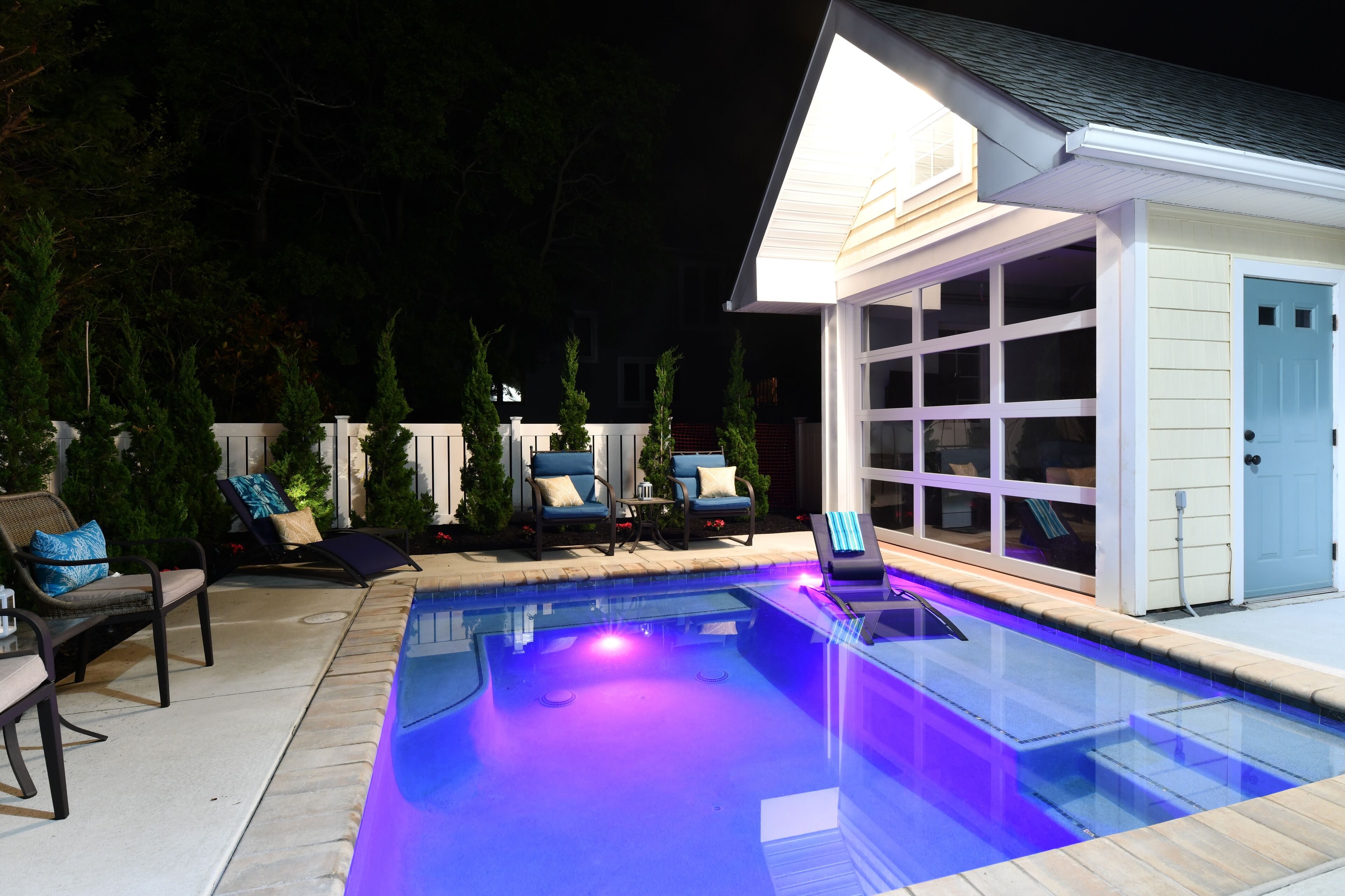 A swimming pool with a clear edge, surrounded by lounge chairs and a small building with large windows.