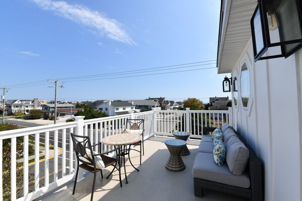 A balcony with a white railing, a round table with chairs, and a sofa with cushions.