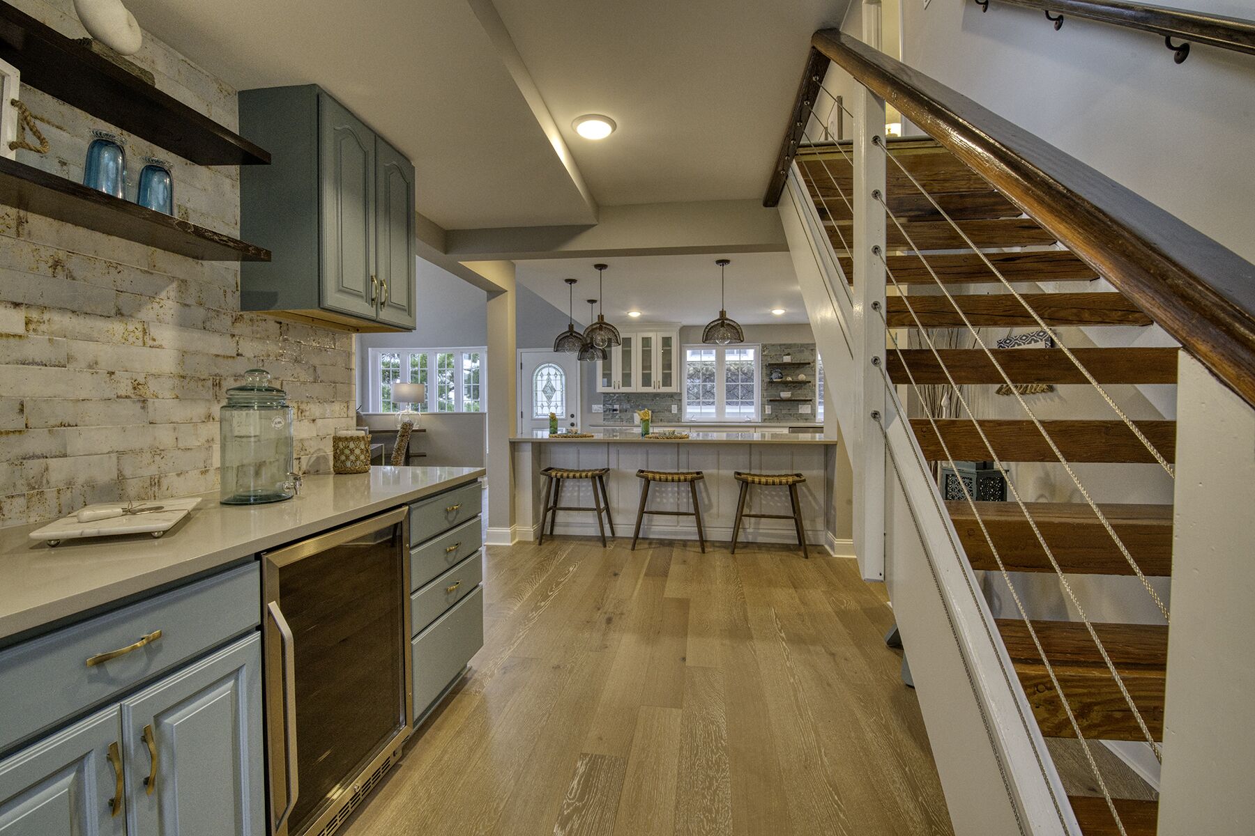 A kitchen with a brick backsplash, wooden floor, and a staircase with a railing.