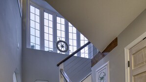Un escalier en bois avec une rampe blanche, menant à un palier d’où l’on peut admirer le paysage extérieur.