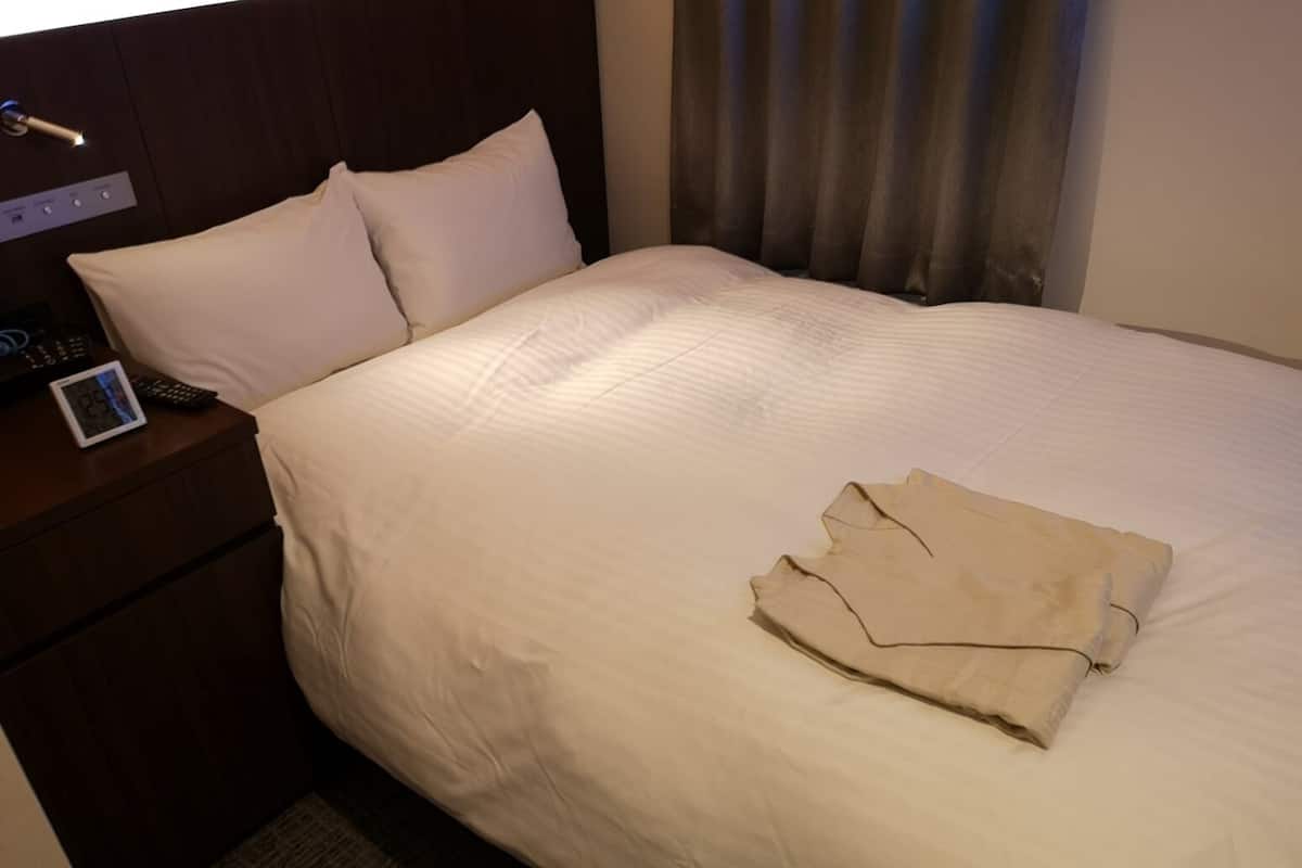 Une chambre d’hôtel avec un lit bien fait, une table de chevet avec une lampe et une horloge numérique.