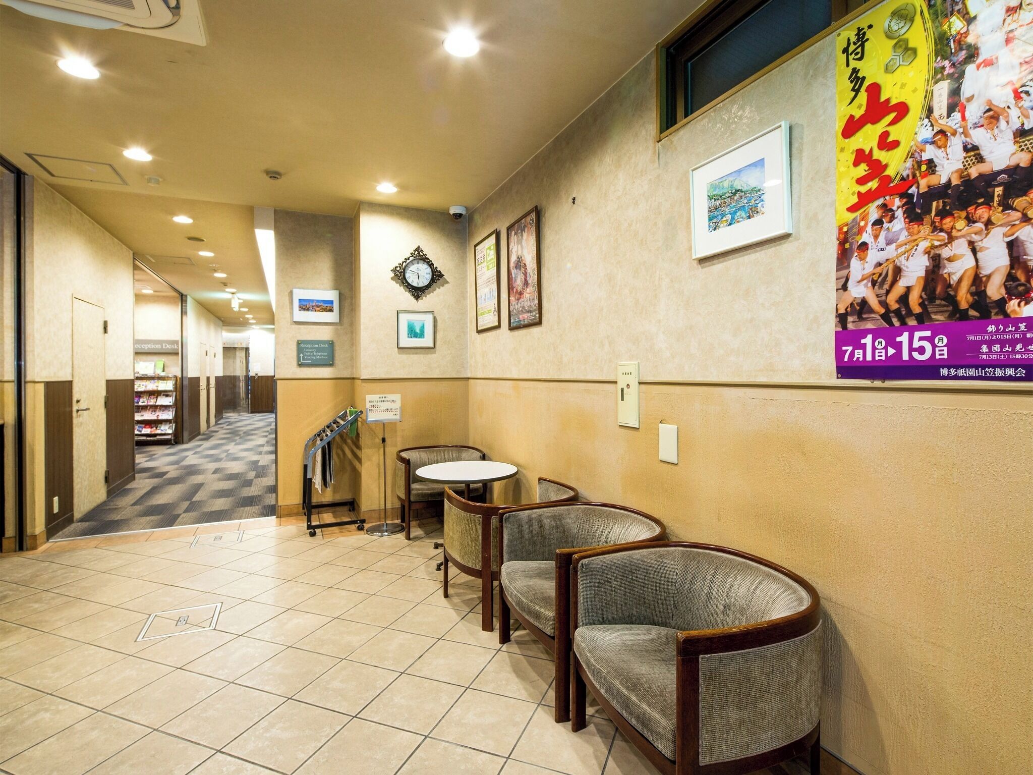 Eine Hotelhalle mit Rezeption, Stühlen, einer Uhr, gerahmten Bildern und einem Poster an der Wand.