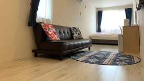 A modern living room with a leather sofa, a patterned rug, and a bed with a white duvet.