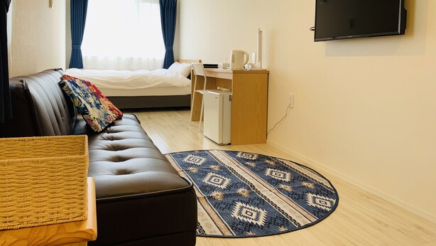 A compact hotel room with a bed, a sofa, a desk, a television, and a patterned rug.