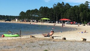 Une plage où l’on voit des gens nager et se détendre, un kayak vert et un parasol rouge.
