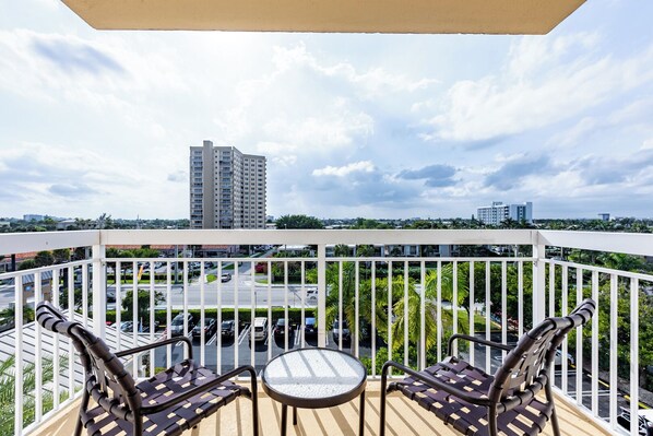 Ein Balkon mit Blick auf eine Stadtlandschaft, darunter ein hohes Gebäude und ein Parkplatz.