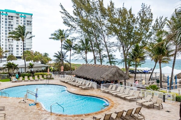 A resort pool area with lounge chairs, a thatched-roof hut, and a view of the ocean.