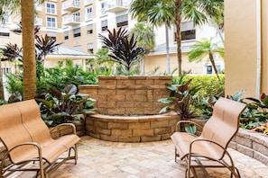 A courtyard with a stone fire feature, two wicker chairs, and lush tropical plants.