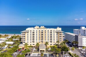 A multi-story hotel with a central courtyard, parking lot, and a view of the ocean.