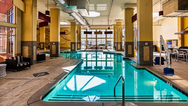 An indoor swimming pool with multiple lanes, seating areas, and a view of the outside.