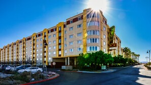 A multi-story hotel with a central courtyard, parking lot, and palm trees.