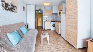 Een knus woongedeelte met een bank, een kleine tafel, een wasmachine en een keuken.