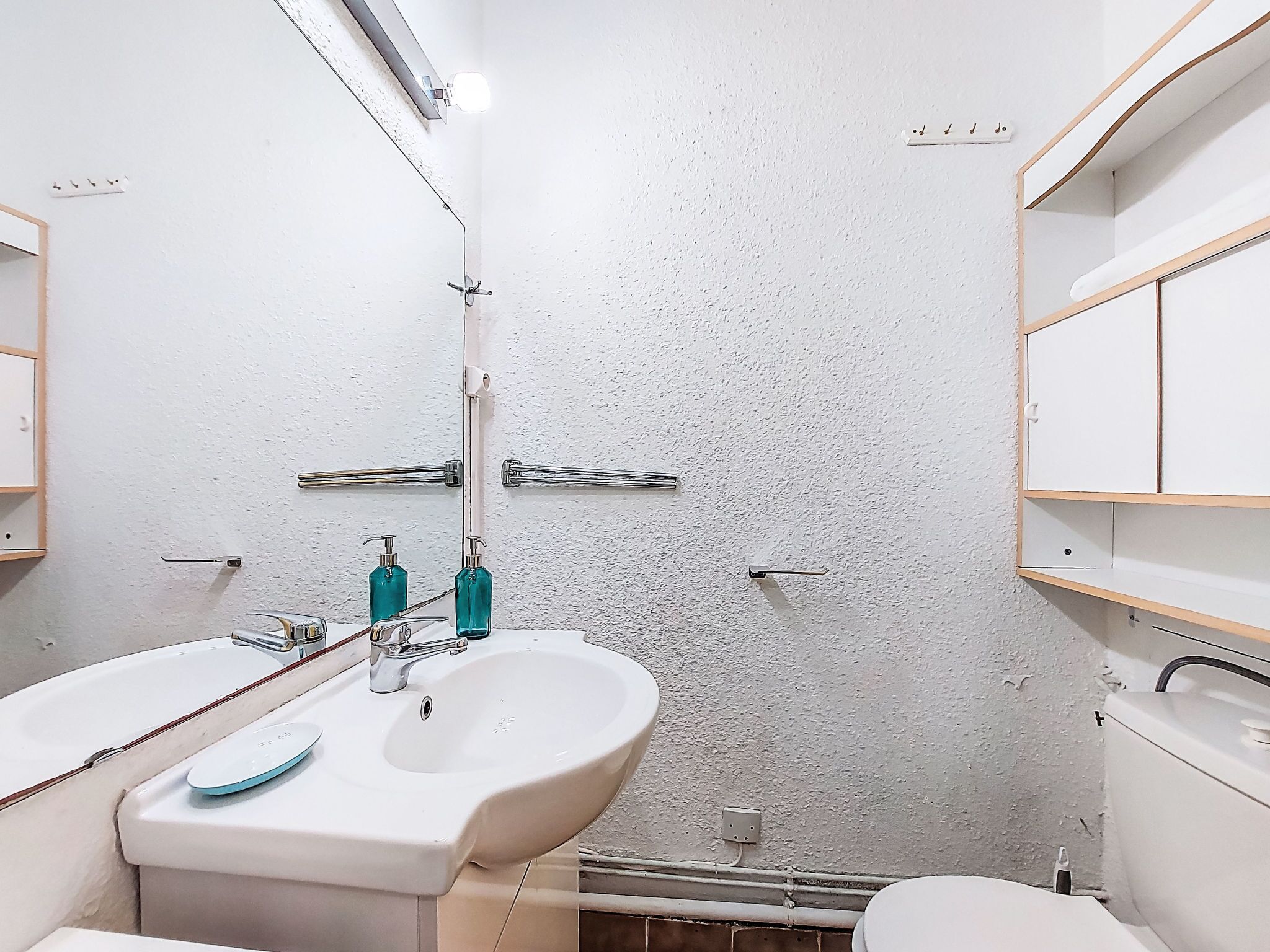 Ein Badezimmer mit weißer Wand, zwei Waschbecken mit Wasserhähnen und einem Spiegel über dem Waschbecken.
