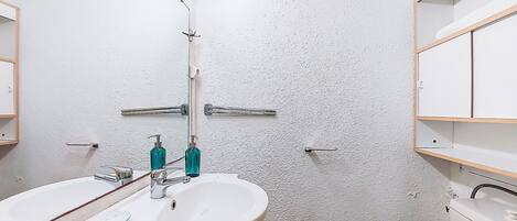 Ein Badezimmer mit weißer Wand, zwei Waschbecken mit Wasserhähnen und einem Spiegel über dem Waschbecken.