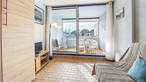 Een knus woongedeelte met een bank, een televisie, een boekenkast en een eethoek met stoelen en een tafel.