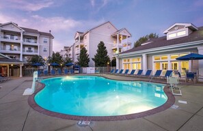 A swimming pool surrounded by lounge chairs and umbrellas, with buildings in the background.