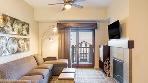 A living room with a sofa, a fireplace, a television, and a balcony with a view.