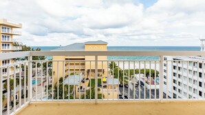 Un balcón con vista a una playa, una piscina y un edificio de varios pisos.