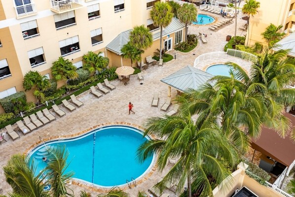A hotel with multiple swimming pools, lounge areas, and palm trees.