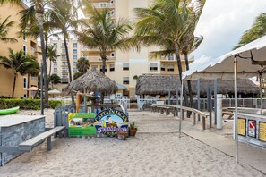 A beach area with a sign for Captain Jack's Oceanfront, a wooden bench, and a thatched-roof structure. - Pompano Beach | Couples Ocean Coast Retreat | Pool + Beach (Pompano Beach)