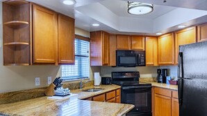 Una cocina con armarios de madera, encimera de granito, microondas negro, estufa y refrigerador.