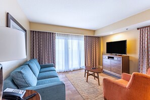 Ein Hotelzimmer mit Sofa, Sessel, Fernseher und Schreibtisch mit Telefon.