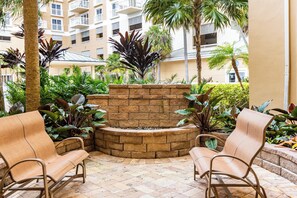 A courtyard with a stone fire feature, two wicker chairs, and lush tropical plants.