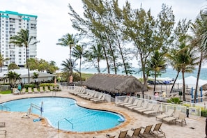 A resort pool area with lounge chairs, a thatched-roof hut, and a view of the ocean. - Pompano Beach | Couples Ocean Coast Retreat | Pool + Beach (Pompano Beach)