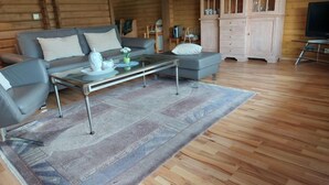 A cozy log cabin interior with a grey sofa, a glass coffee table, and a wooden cabinet with glass doors.