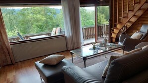 A modern living room with a glass coffee table, leather sofa, and a view of a balcony with a wooden railing.