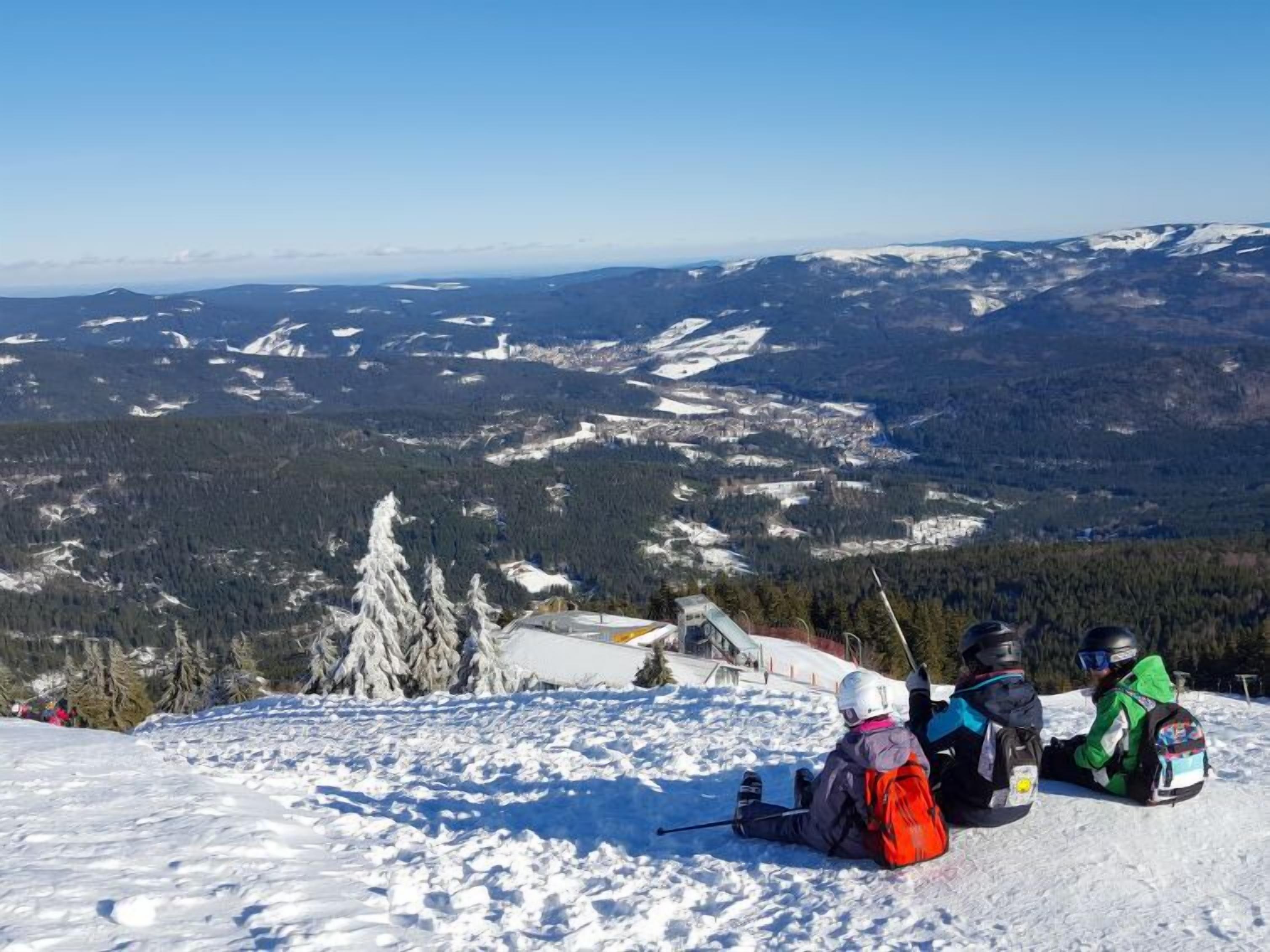 A snowy mountain landscape with a ski slope and a group of people sitting on the slope.