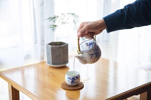 A hand pouring tea from a teapot into a cup on a wooden table. - JiuYueJi Inn (Hangzhou)